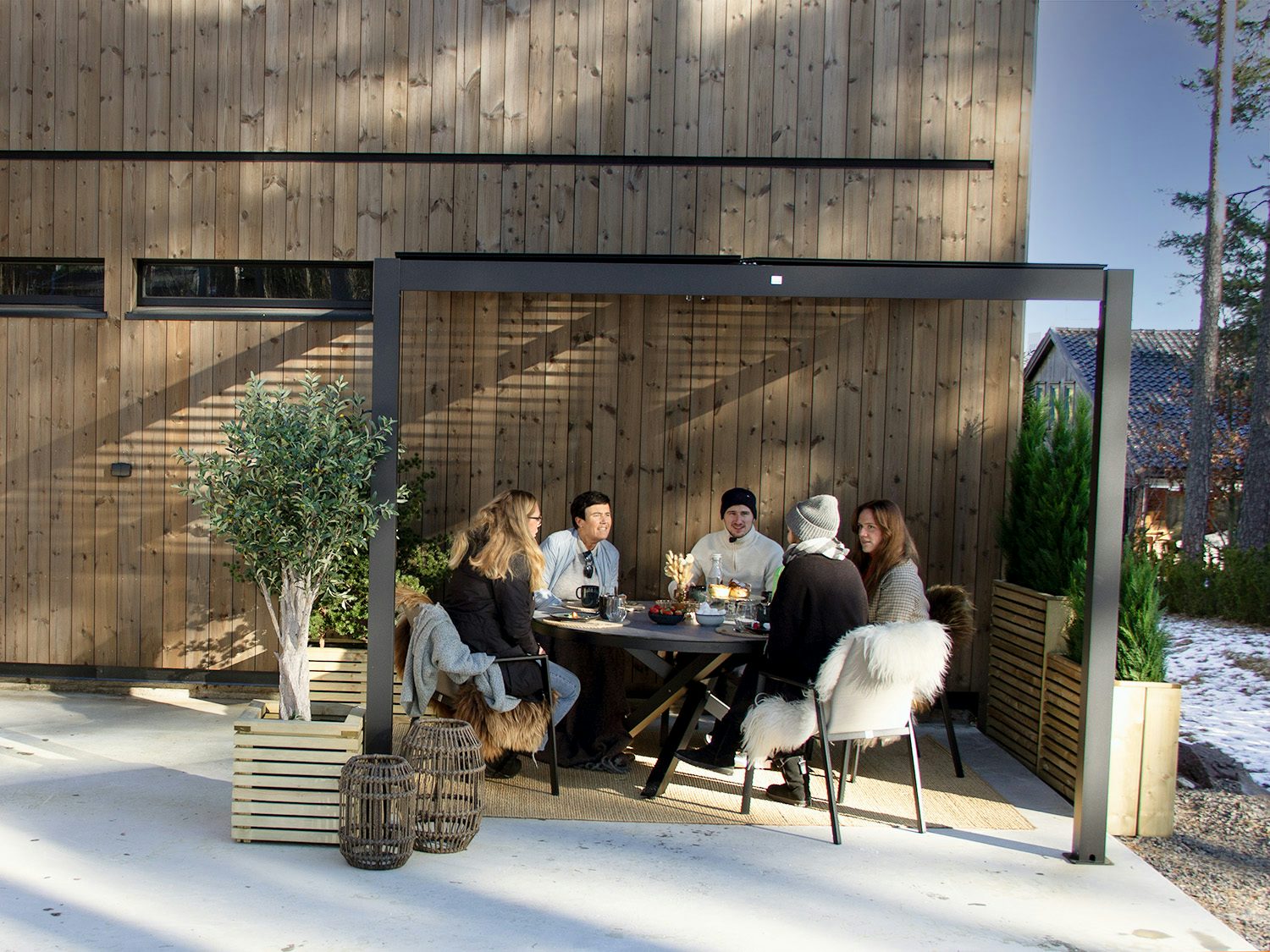 en gruppe mennesker som sitter ute under en vegghengt pergola på våren