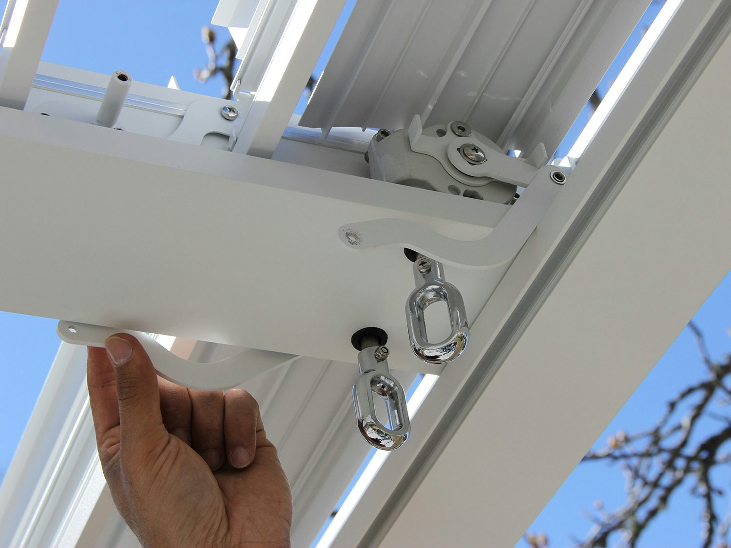 hånd som viser hva man skal løsne på pergola for å sette på lameller. Foto