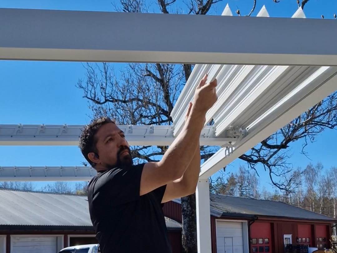 Mann monterer lameller på hvit pergola