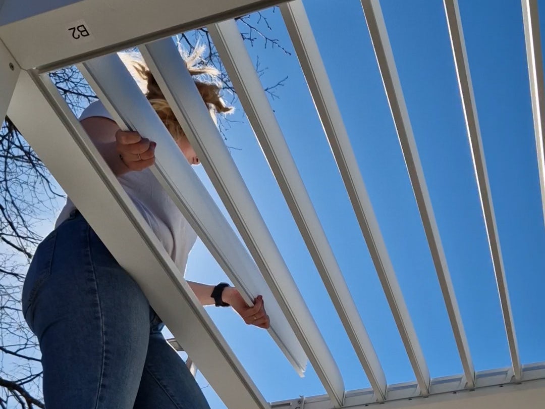En person som setter på lameller på en hvit pergola